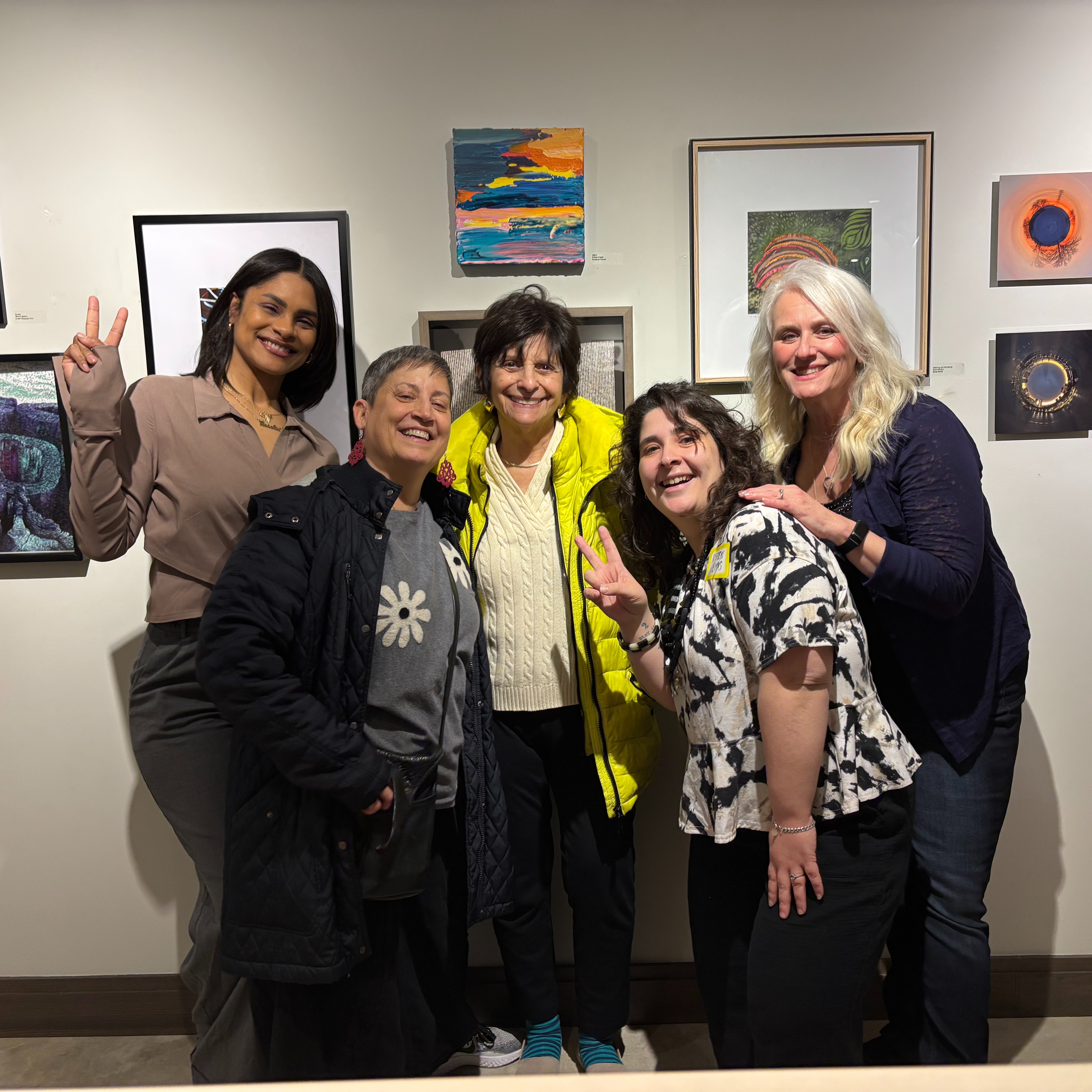 Five women (artists) posing in front of a variety of artwork displayed at ClipArt Gallery.