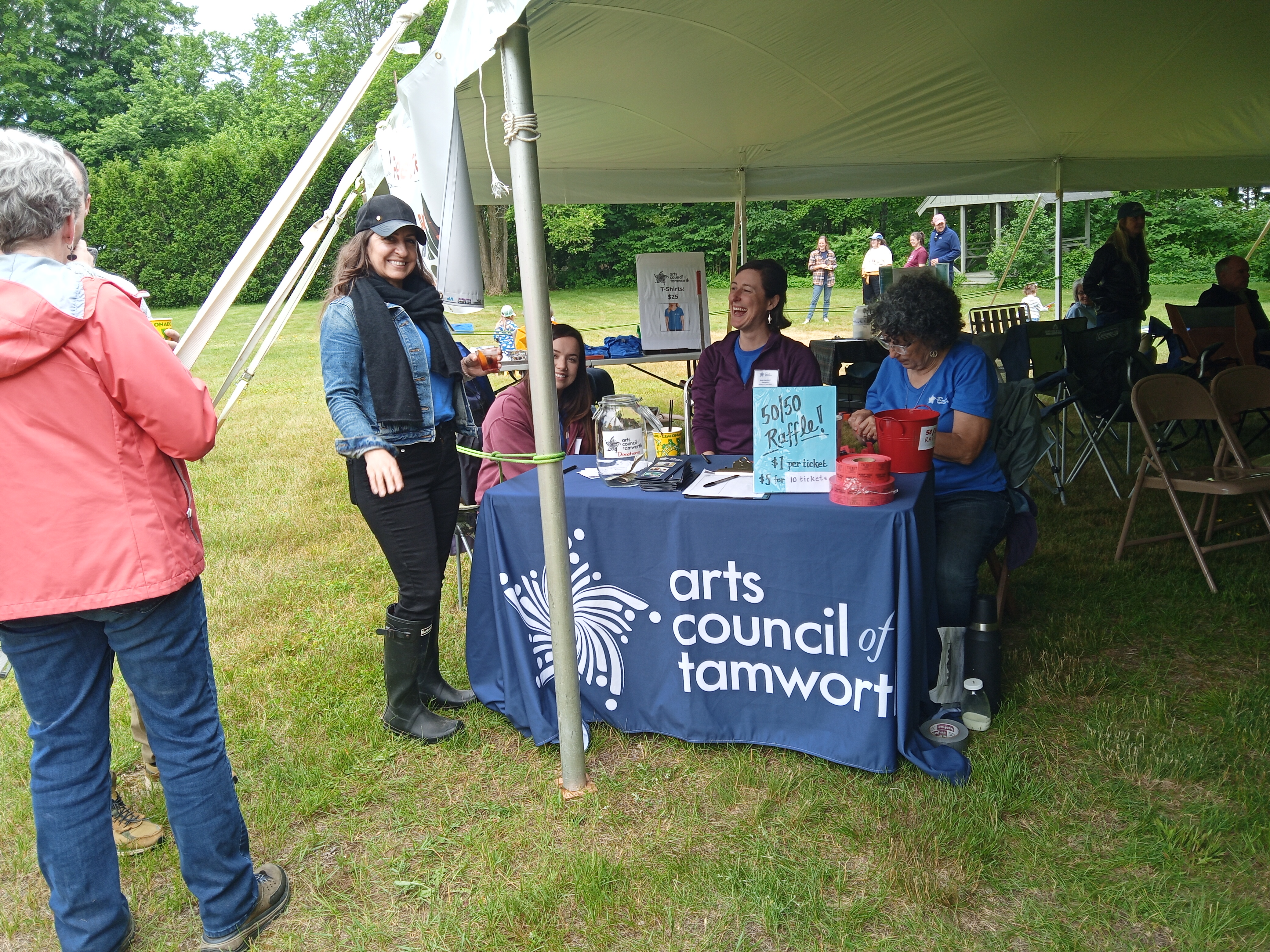 Three women are sitting, and one woman is standing, at a table with a navy blue tablecloth with the words "Arts Council of Tamworth."