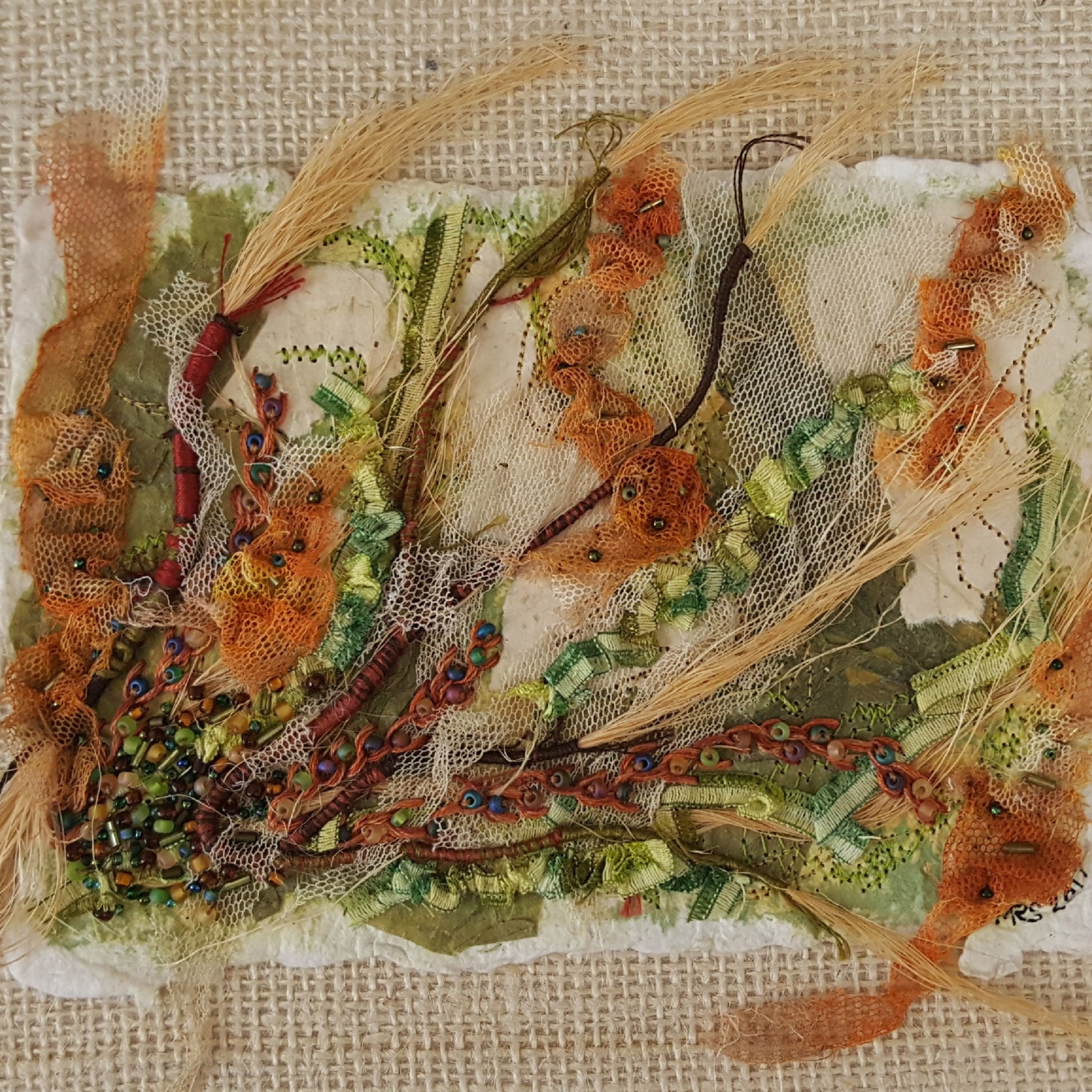 A yellow textured paper with brown and gold embroidery, green beads and gathered netting