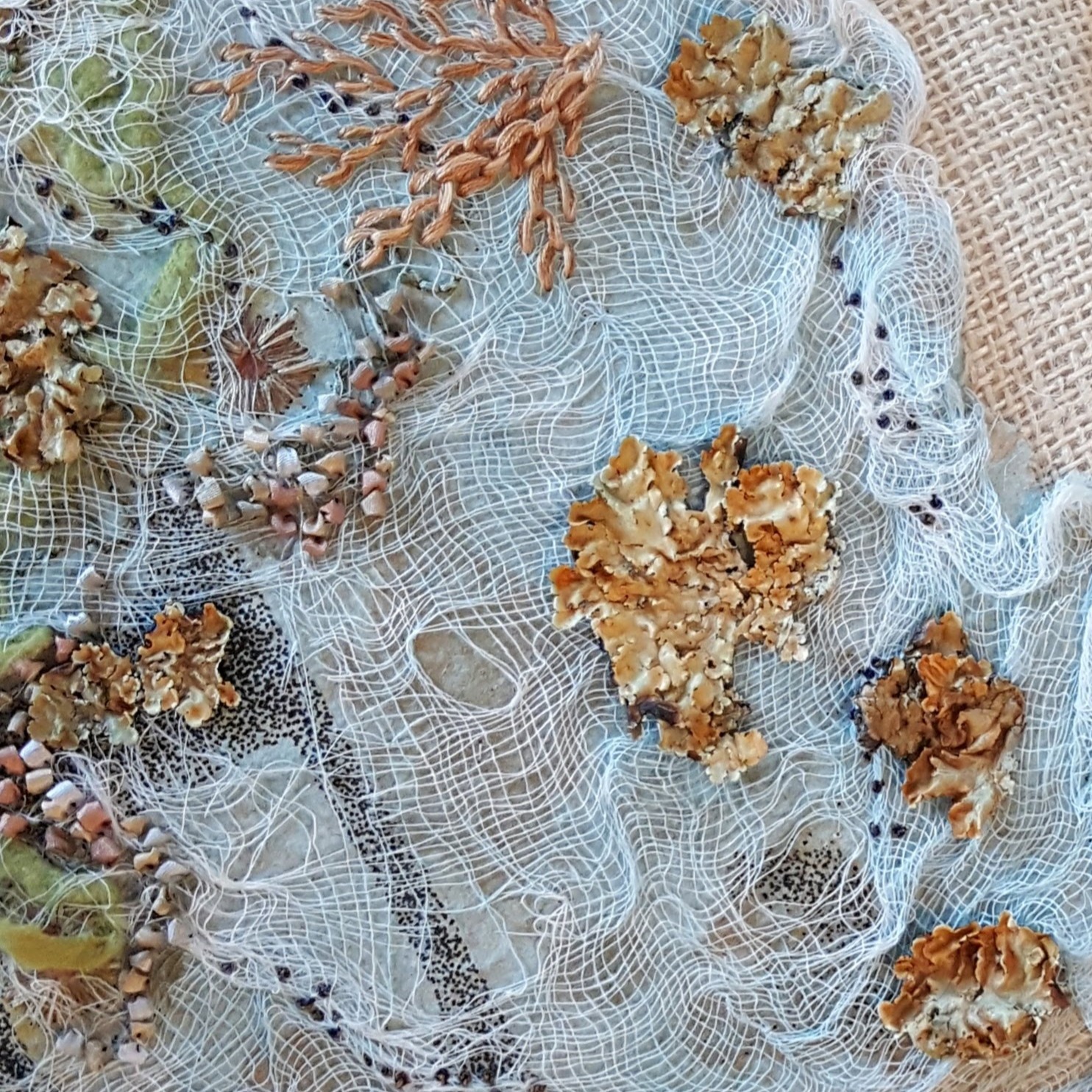 A textured surface with a light blue background and embroidery of golds and greens