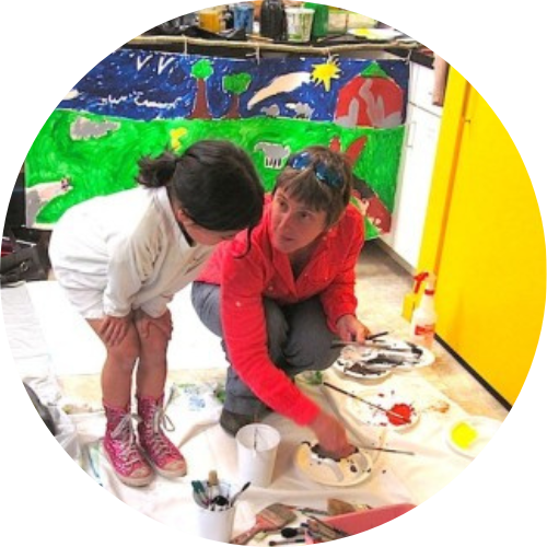 Teaching artist crouching down next to child looking at buckets of paint and brushes