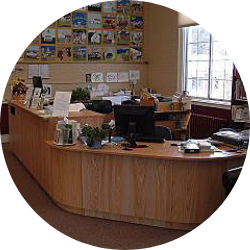 The circulation desk at the Goshen Public Library has a computer and lots of shelves with books and pamphlets