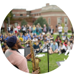 a black man plays saxophone on a lawn in front of a large crowd