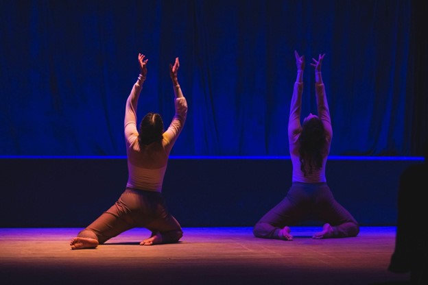 Dancer on their knees facing away from the camera, arms and body reaching towards the ceiling